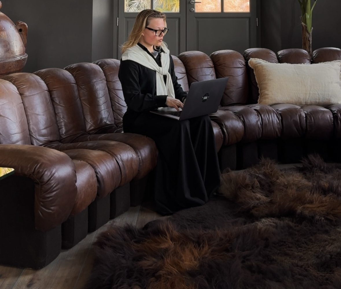 Emma working on her laptop on a leather sofa under a chandelier